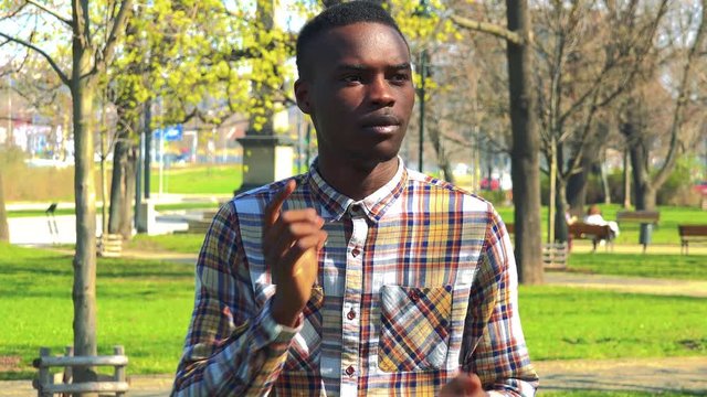 A young black man covers his eyes with his hands, stops and looks around in confusion - a park in the background