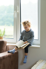 Young caucasian boy with curly hair reading book