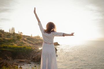 young woman walking on the morning beach in beautiful white dress. Fit female having good time during turing the sunrise.