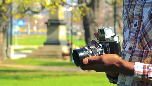 A black man holds a camera in his hands in a park on a sunny day - closeup