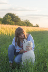 portrait of woman and white puppy of husky dog in the fields, green grass and sunset background