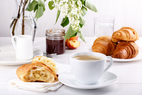 Breakfast - cup of coffee, croissants, jam and fruits on white table.