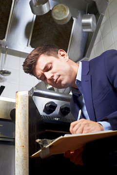 Health Inspector Looking At Oven In Commercial Kitchen