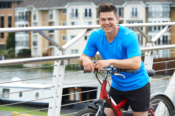 Young Man Cycling Next To River In Urban Setting