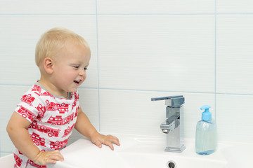 Close-up portrait of cute white Caucasian boy toddler one year old washing hands in bathroom and looking surprised excited, playing with water