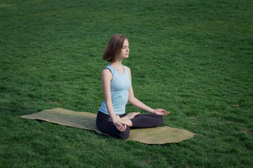 Young fit yoga  woman meditating and relaxing in lotus on the  green grass, city park background 