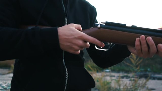 man in a black hood charges a rifle, takes aim and makes a shot, close-up, slow motion