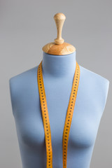 Blue tailor dummy with measuring tape alongside the wall.