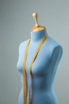 Blue tailor dummy with measuring tape alongside the wall.