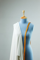 Blue tailor dummy with measuring tape alongside the wall.