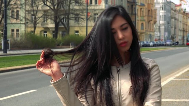 A young Asian woman is bored and plays with her hair in the middle of a street in an urban area