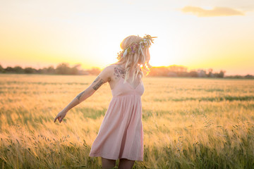 Fototapeta na wymiar beautiful blonde lady in head flower wreath during sunrise in summer wheat fields 