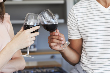 Couple toasting with red wine in kitchen, close up