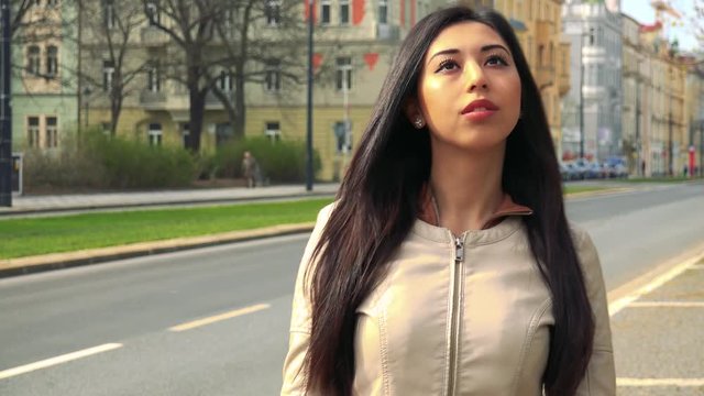 A young Asian woman covers her eyes with her hands, then stops and looks around in confusion - an urban area in the background