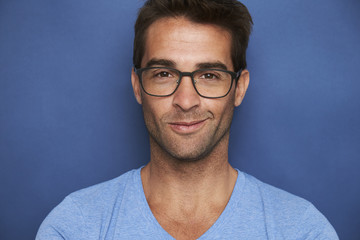 Obraz premium Handsome guy in glasses smiling in blue studio