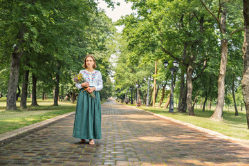 young women in vintage retro style linen dresses with bouquet of flowers on a park road