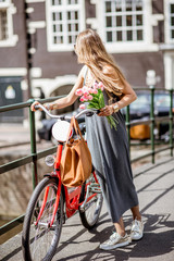Young beautiful woman standing with red bicycle and bouguet of tulips on the bridge over the water channel in Amsterdam old city
