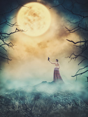 Beautiful woman with crow on the rock against spooky sky. Halloween scene