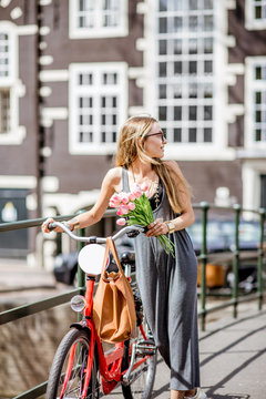 Young beautiful woman walking with red bicycle and bouguet of tulips on the bridge over the water channel in Amsterdam old city