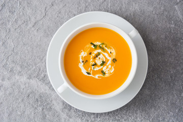 Pumpkin soup in white bowl on gray stone
