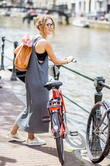 Fototapeta premium Młoda i piękna kobieta z torbą i kwiatami, spacery z rowerem na kanale wodnym w mieście Amsterdam