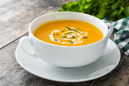 Pumpkin soup in white bowl on wooden table
