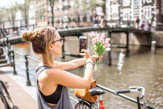 Young woman photogarphing with phone beautiful bouquet of pink tulips on the city background in Amsterdam