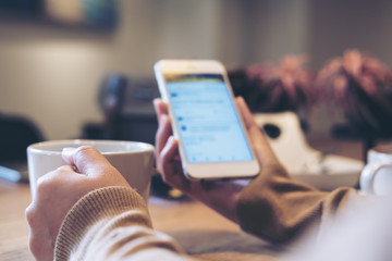 A woman's hands holding white coffee cup and mobile phone while using social media in modern loft...
