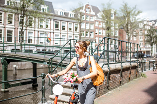 Young beautiful woman walking with red bicycle and bouguet of tulips near the water channel in Amsterdam old city