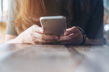 Closeup image of a woman's hands holding and using at smart phone on wooden table in vintage cafe