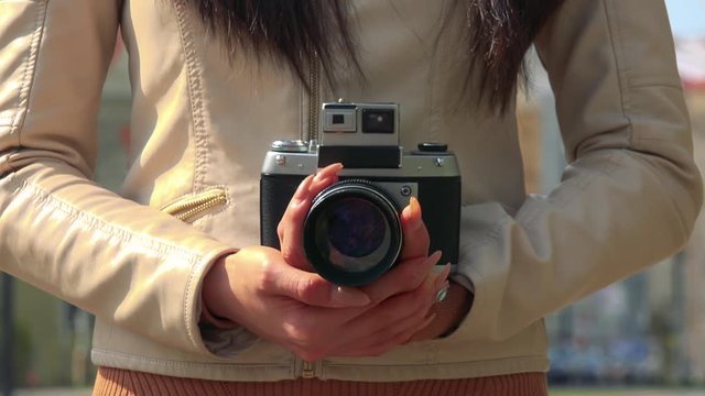 An Asian woman holds a camera - closeup - an urban area in the blurry background