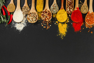 Spices in wooden spoons on black background.