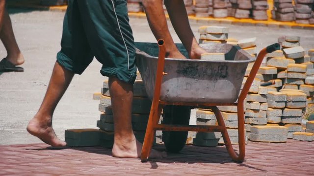 Construction Site, the Construction Worker Unloads the Stone Paving from the wheelbarrow. Slow Motion in 96 fps. Building Process, Repairing Sidewalk. Worker Laying Stone Paving in a city Park. Road