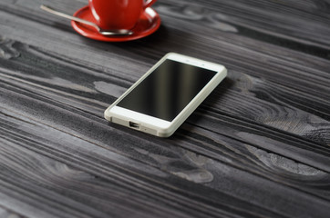 White smartphone and red cup of coffee on dark wooden table. Coffee break concept