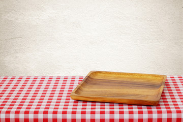 Empty wooden tray on red checked tablecloth over brown cement wall background, kitchen utensil, food display montage