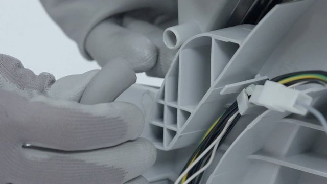 A man is dismantling a dishwasher in order to fix a problem on it. He is wearing safety gloves and is trying to find a problem.