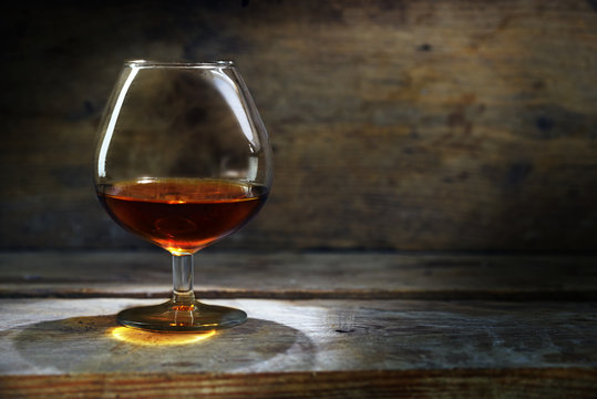 glass with cognac or brandy on warm rustic wood, concept for enjoyment or addiction, selected focus, narrow depth of field