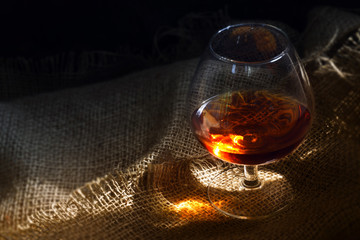 Cognac or brandy in a glass with a glowing light reflex on rustic burlap, concept for enjoyment or...