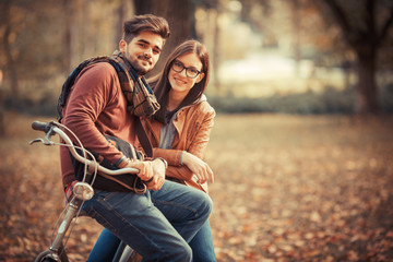 Young couple sitting on bicycle at the park on autumn day.Love and making fun.