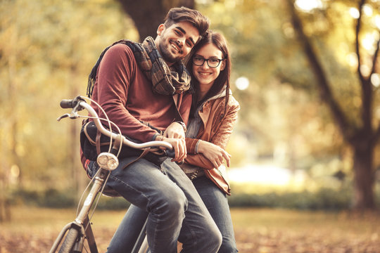 Young couple sitting on bicycle at the park on autumn day.Love and making fun.