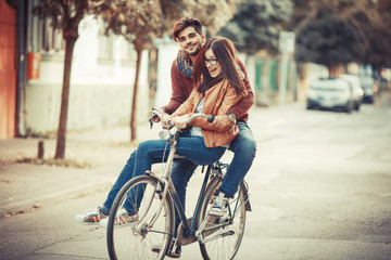 Young couple riding bicycle at the street on autumn day.They sitting on bike and making fun.