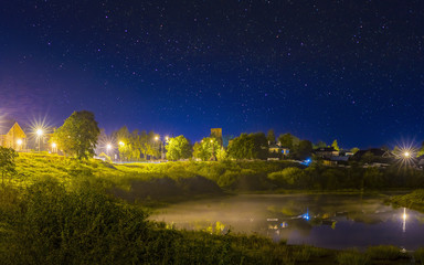 Night landscape of the old town with shining streetlight. Night sky with stars. Misty fog on river.