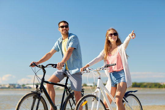 happy young couple riding bicycles at seaside