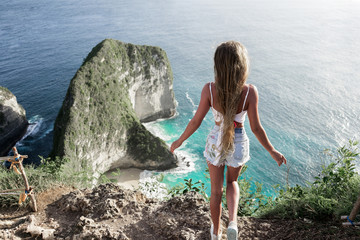 The girl stands on a steep rock and makes a wish