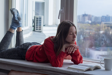 Young woman relzxing with book on window sill