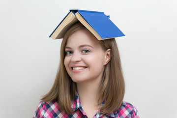 Cute and funny caucasian girl with book on her head, smiling, looks happy
