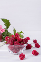 Red fresh raspberries in a glass bowl with green leaves on white background. 