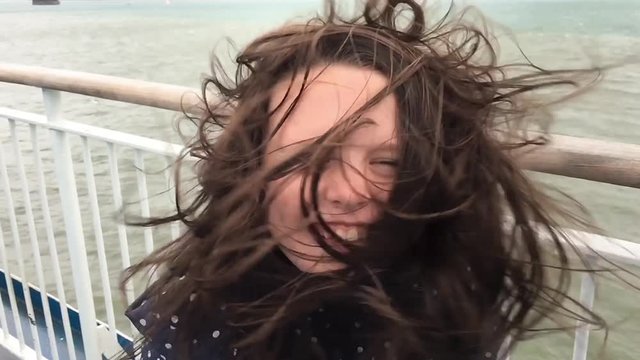 Girl smiling as she stands on a windy ferry deck with hair blowing everywhere. Filmed in slow motion