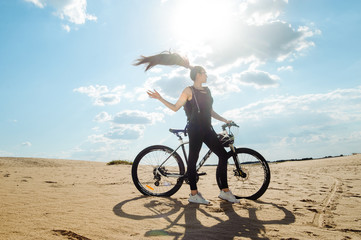 Fototapeta premium Woman cyclist carrying mountain bike on sunrise trail. Girl in sport wear on black white bicycle going to record in summer sunset time in desert.