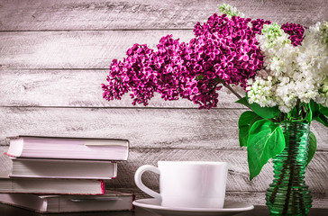 Stack of books, cup of coffee and lilac flowers on wooden background. cover, card. copy space.